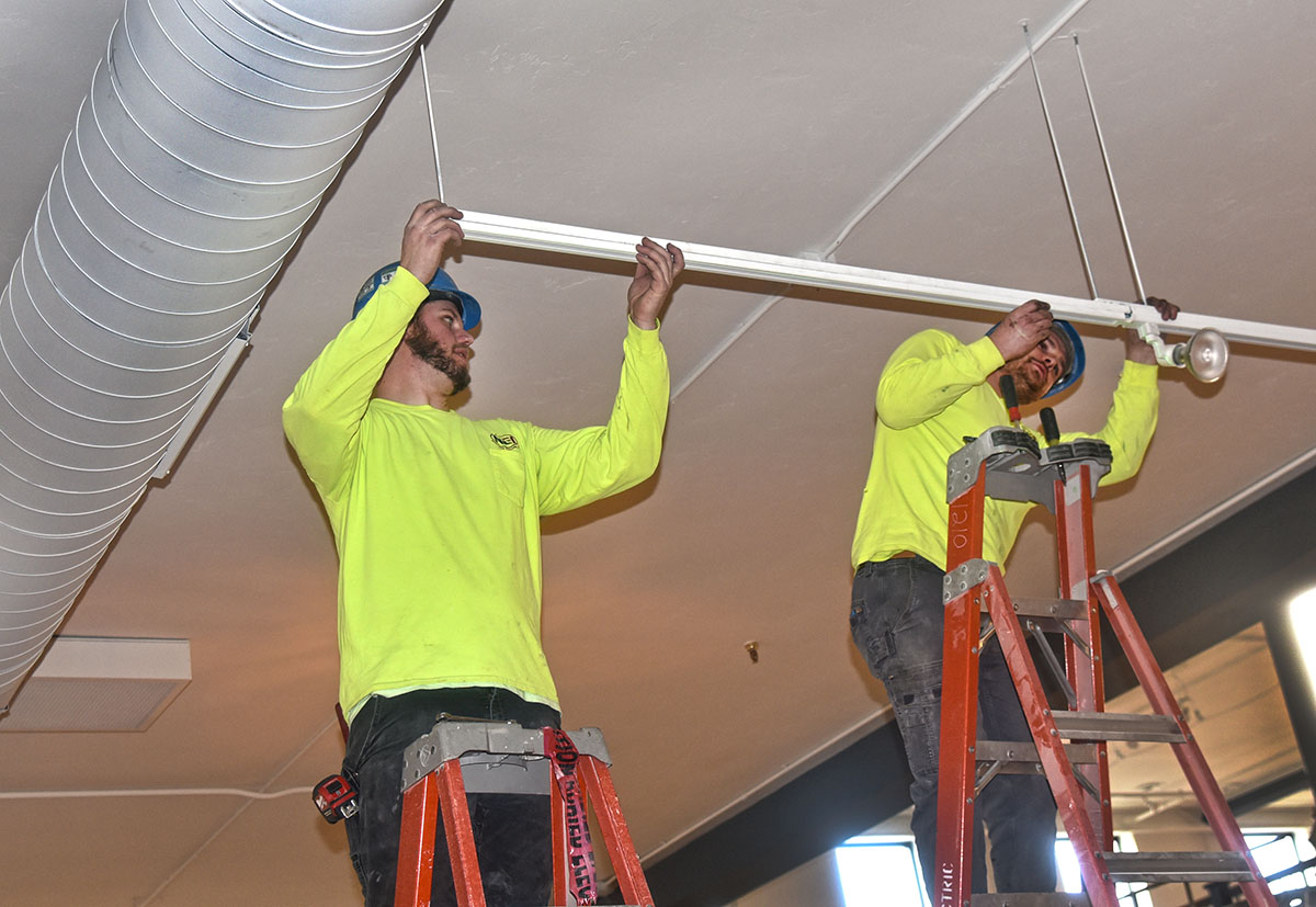 Two electricians installing a track lighting fixture at Bliss in Green Bay, WI