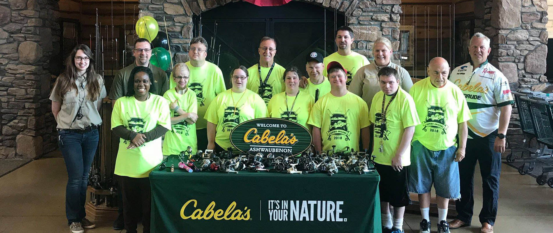 Aspiro Anglers group gathered behind a table full of fishing reels at Cabela's