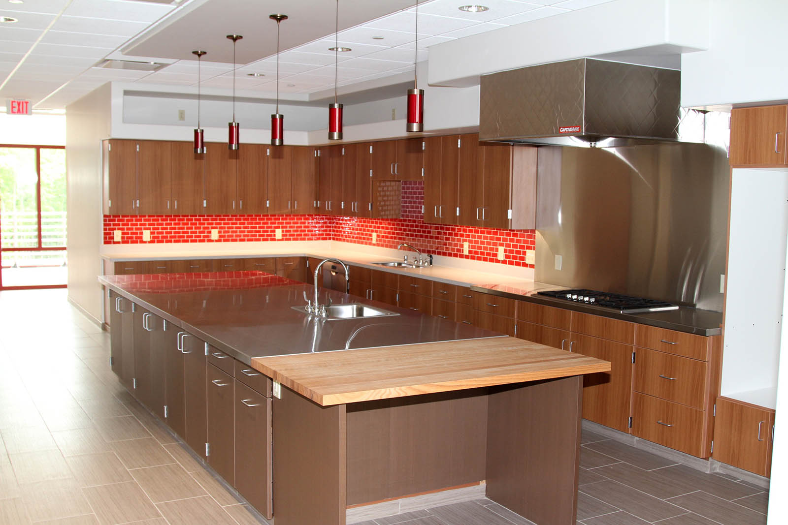 Kitchen area with overhead hanging light fixtures, backsplash lighting and large range hood