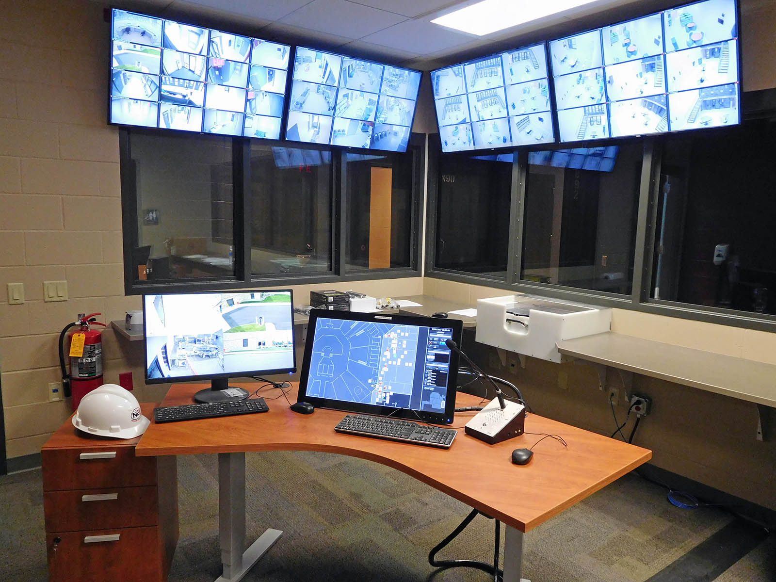 Control room with two computers on a desk, along with 4 large monitors with security camera footage on display