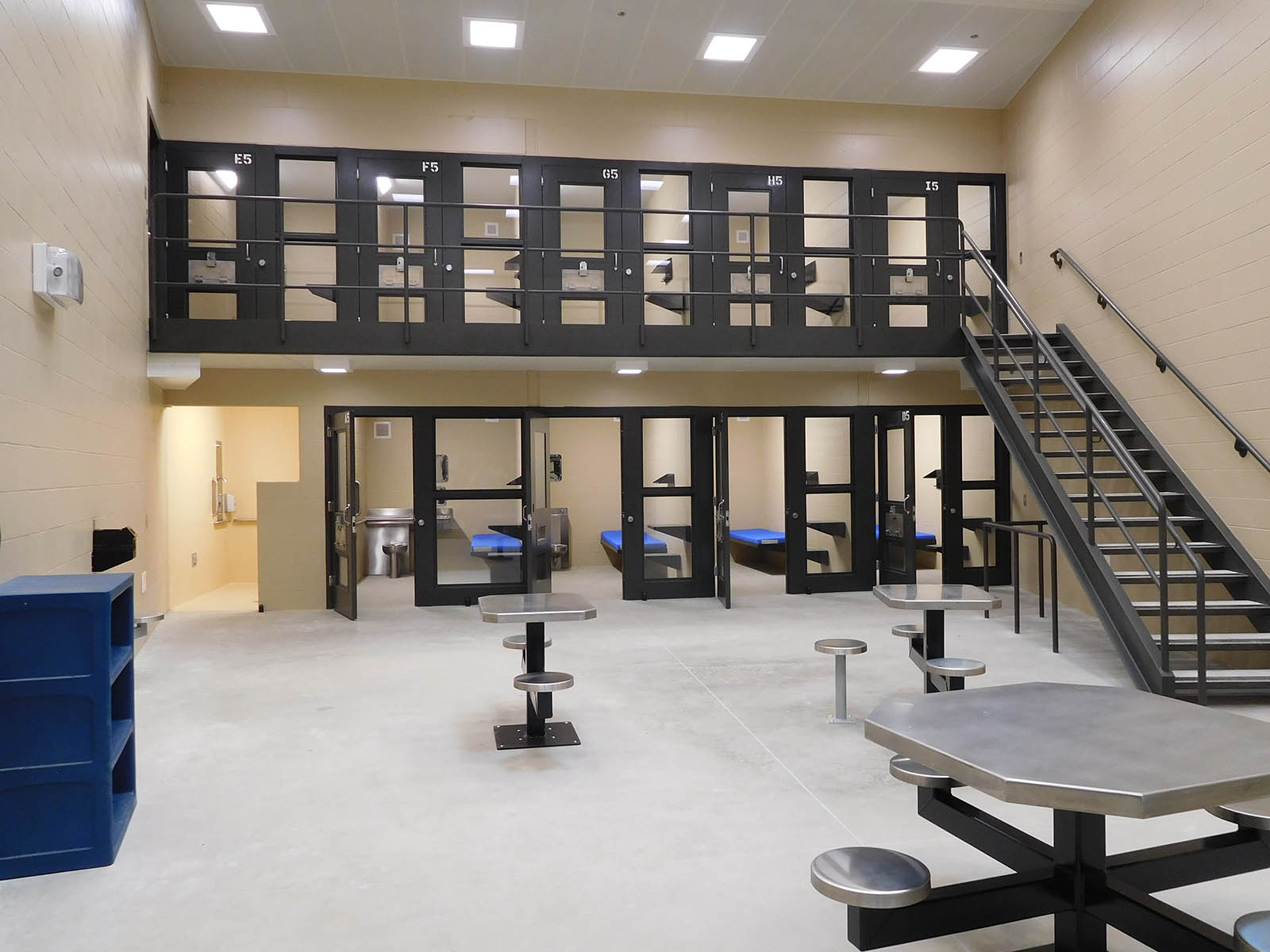 Common area with tables and benches with jail pods with detention doors in background