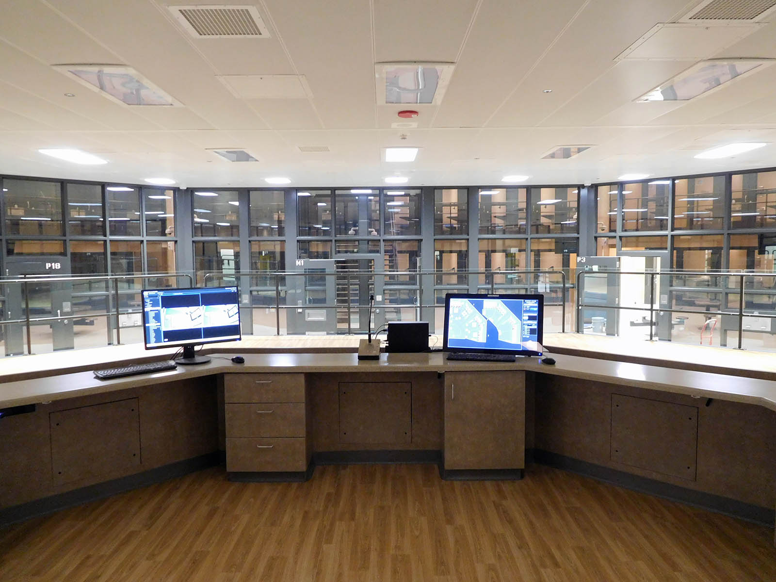 A large desk with two computers on it overlooking the 148-bed jail pod area